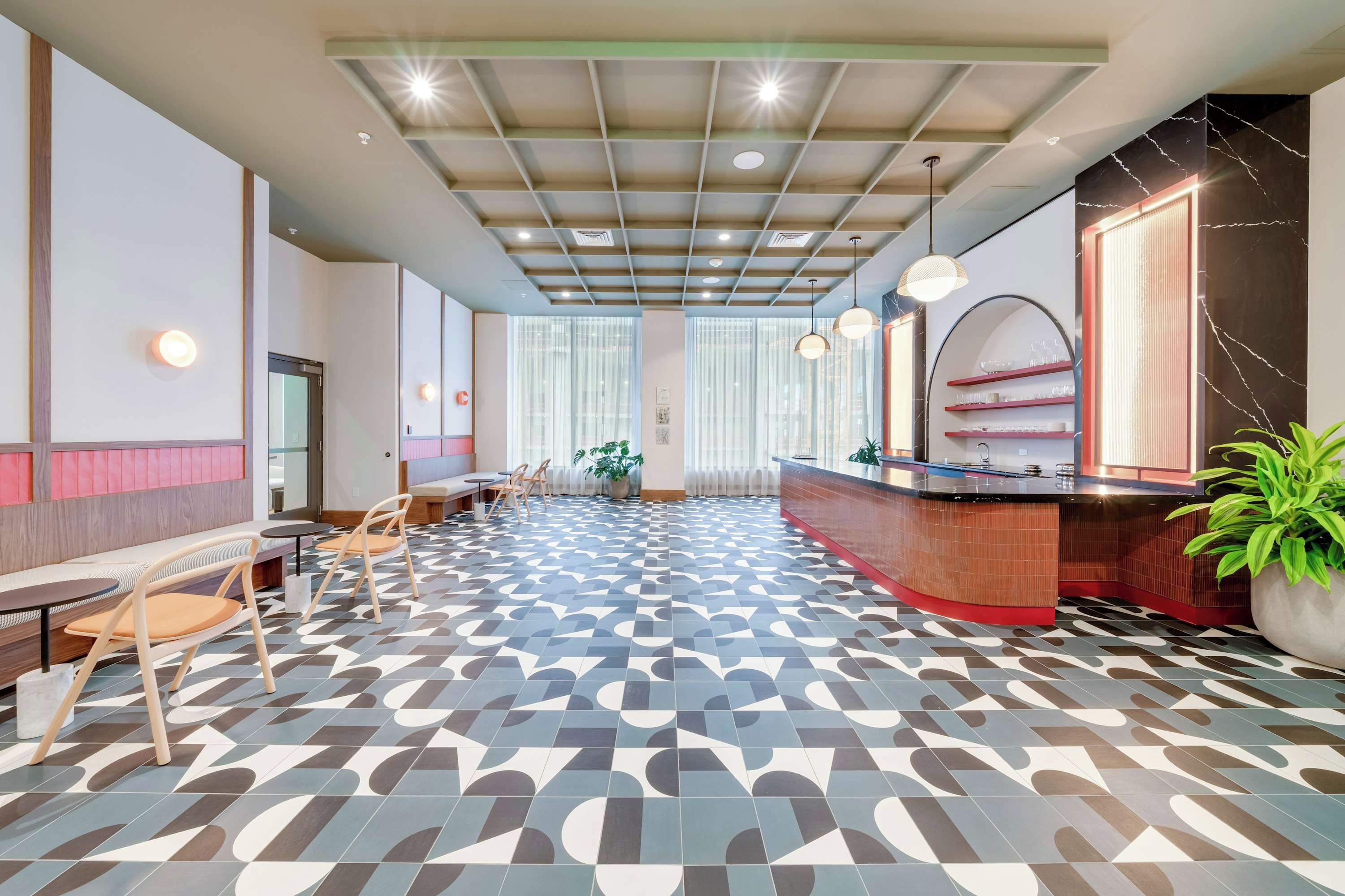 A modern hotel lobby with a patterned floor, seating area, reception desk, and large windows.