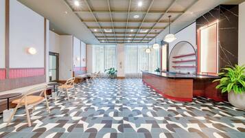 A modern hotel lobby with a patterned floor, seating area, reception desk, and large windows.