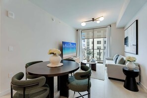 Una sala de estar moderna con una mesa de comedor redonda, sillas tapizadas en verde, un sofá y un ventanal con vistas a edificios.