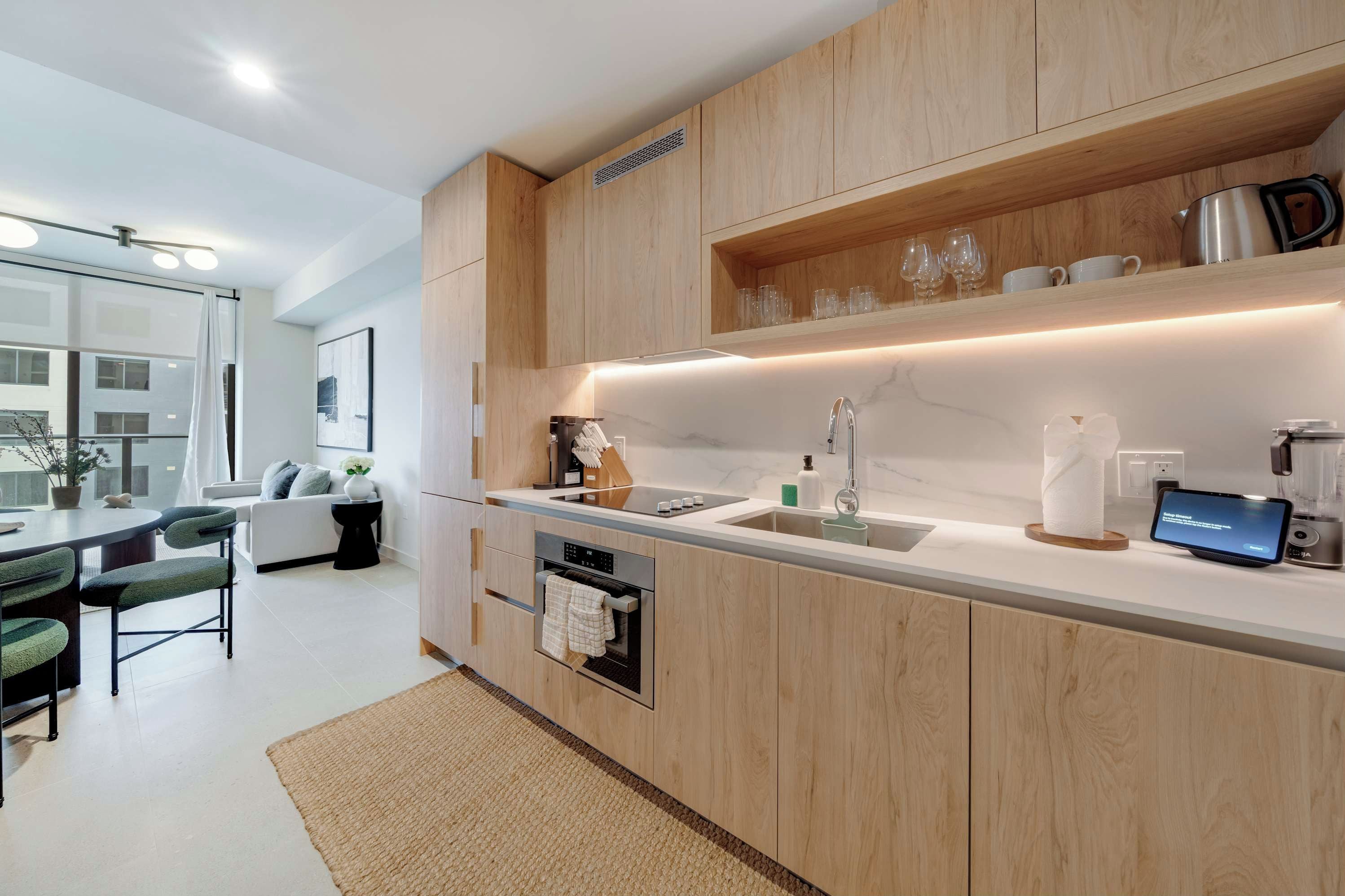 Une cuisine moderne avec des meubles en bois, un four encastré, un évier et un écran numérique.