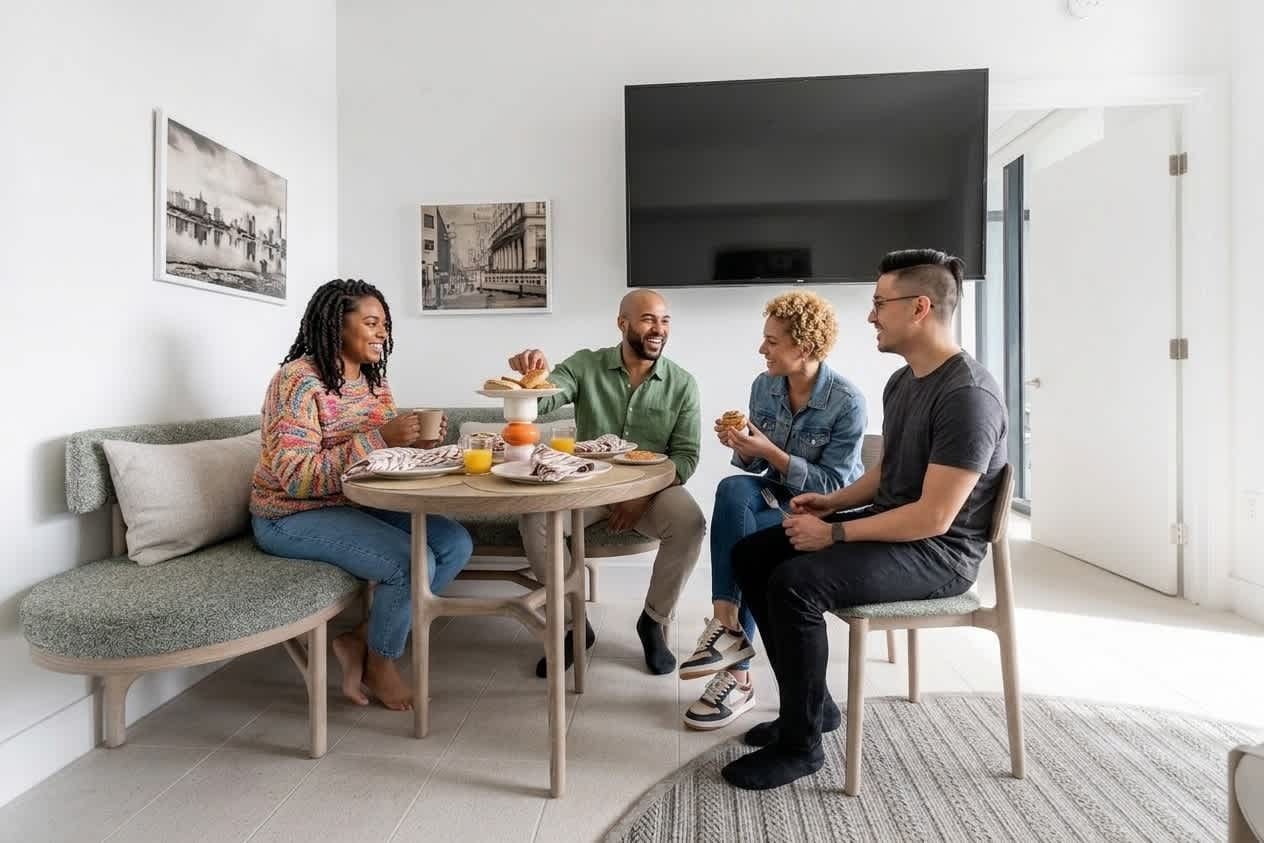 Un groupe de quatre personnes est assis autour d’une table ronde dans un salon moderne, avec un canapé et un téléviseur à écran plat fixé au mur.