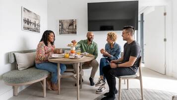 Un groupe de quatre personnes est assis autour d’une table ronde dans un salon moderne, avec un canapé et un téléviseur à écran plat fixé au mur.