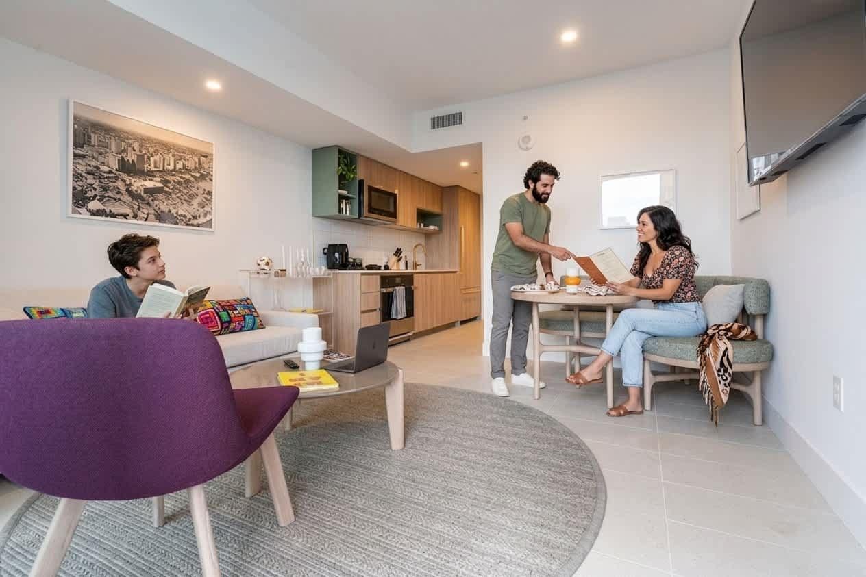 Un salon moderne avec un canapé, une table basse et une table à manger. On aperçoit au fond une cuisine équipée de placards et d’un four à micro-ondes.