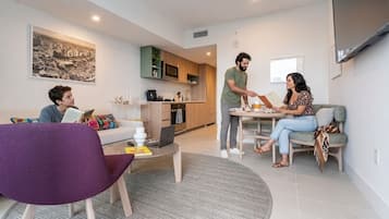Un salon moderne avec un canapé, une table basse et une table à manger. On aperçoit au fond une cuisine équipée de placards et d’un four à micro-ondes.