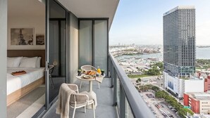 Varanda com cama, mesa de jantar e cadeiras, vista para a cidade e para o mar.