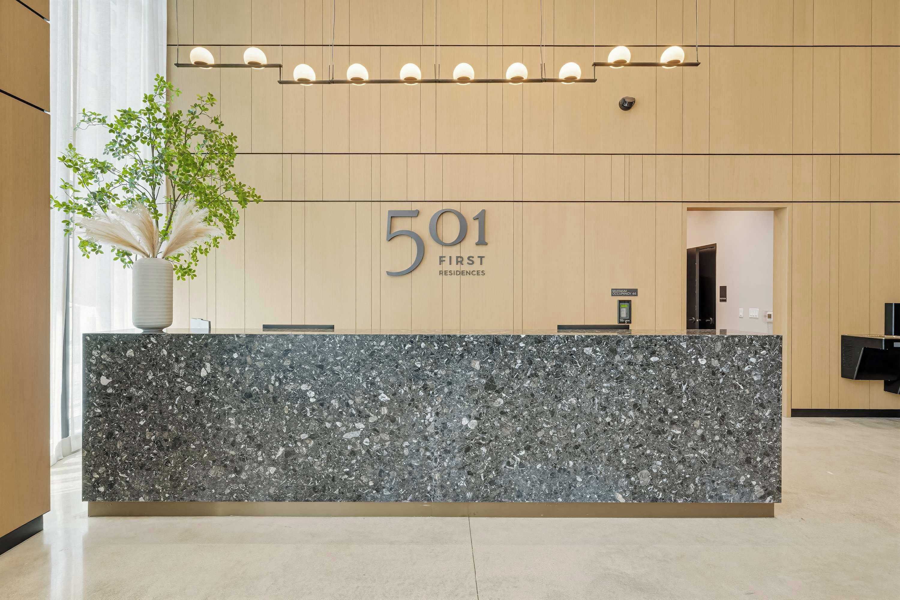 Un mostrador de recepción con encimera de mármol, una planta en maceta y un letrero que dice '501 First Residences'.