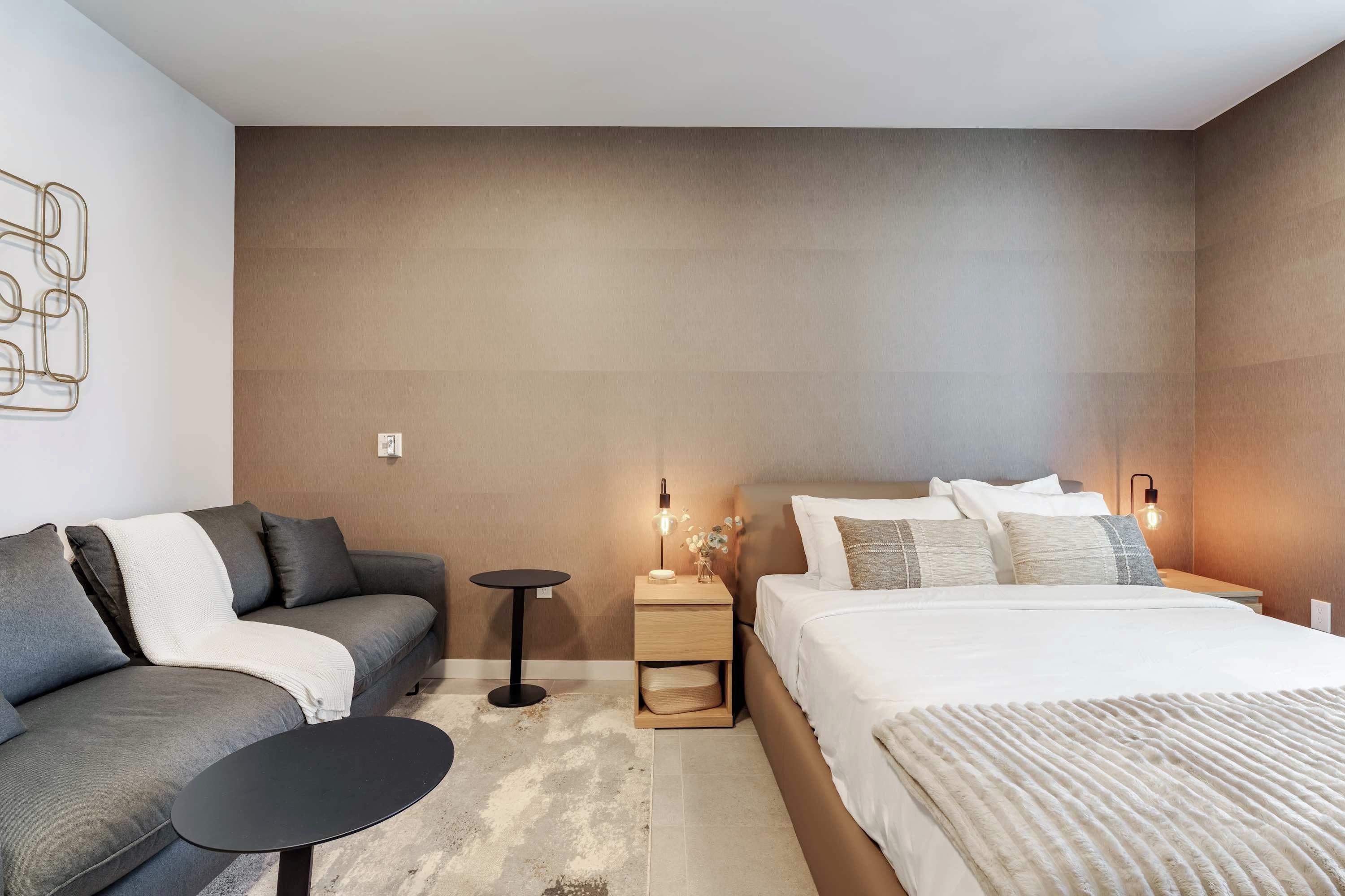 A modern bedroom with a sofa, a bed, a nightstand, and a small table.