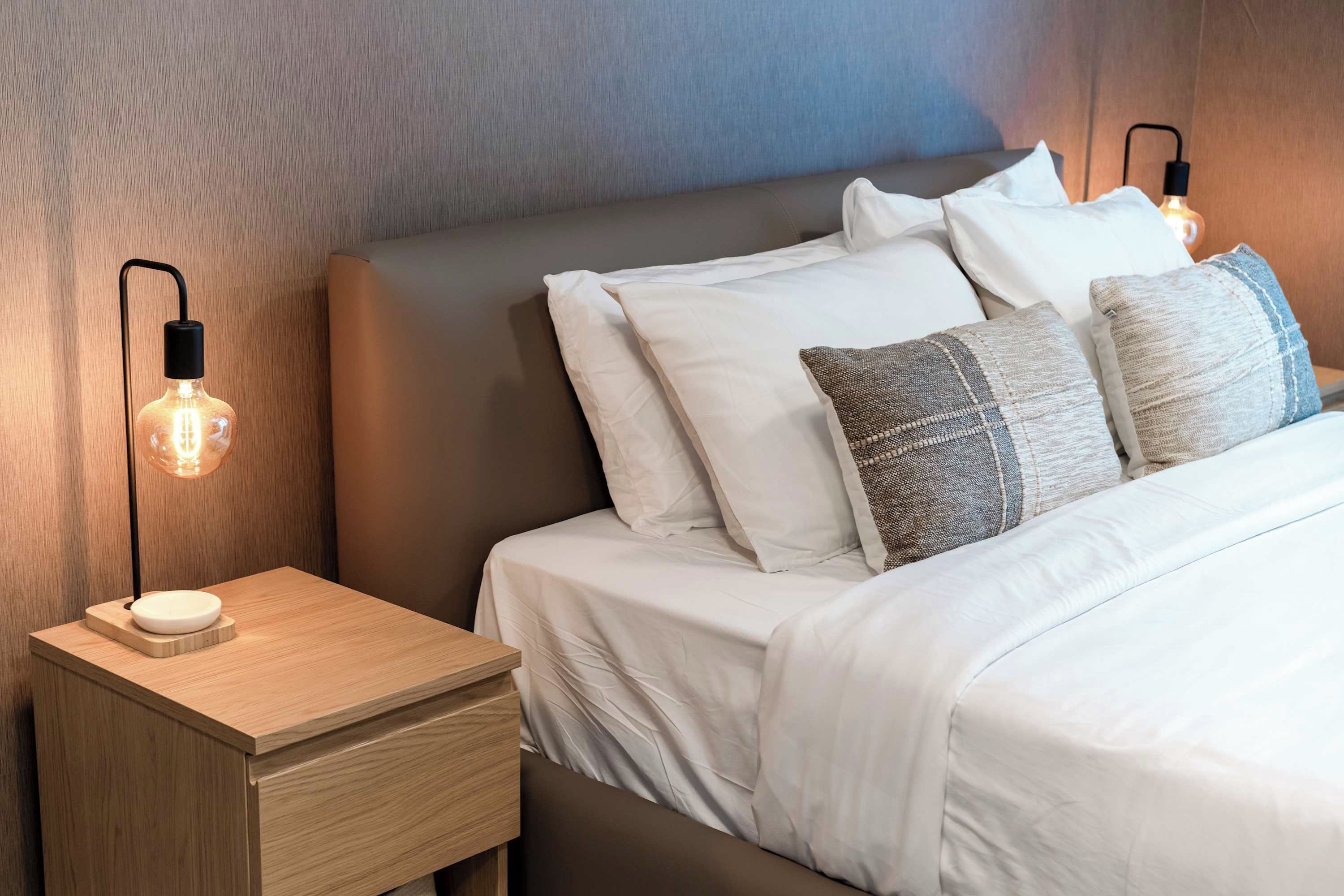 Ein ordentlich bezogenes Bett mit weißer Bettwäsche, ein Nachttisch mit Lampe und ein Kopfteil.