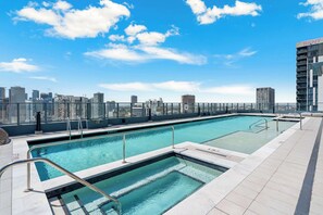 Ein Pool auf dem Dach mit Blick auf die Stadtlandschaft, einer Glasuhr und einem wolkenlosen Himmel.