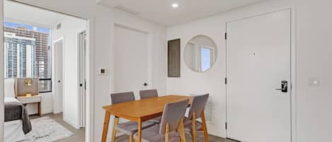 Une chambre moderne avec une table à manger en bois, des chaises grises, un miroir rond et un lit donnant sur la ville.