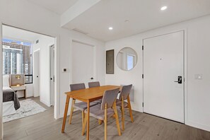 Ein modernes Zimmer mit einem Holzesstisch, grauen Stühlen, einem runden Spiegel und einem Bett mit Blick auf die Stadt.