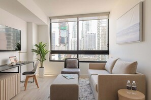 A modern living room with a large window, a sofa, a coffee table, a desk with a laptop, and a plant. - City Dreams Sauna, Rooftop Pool & Parking (Miami)