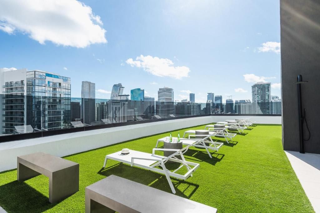 Terraza en la azotea con césped artificial, sillones blancos y mesas, con vistas al horizonte de la ciudad.