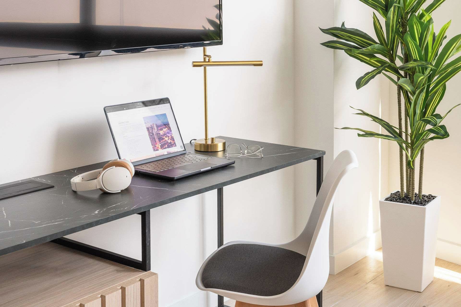 A modern workspace with a laptop, headphones, and a plant.