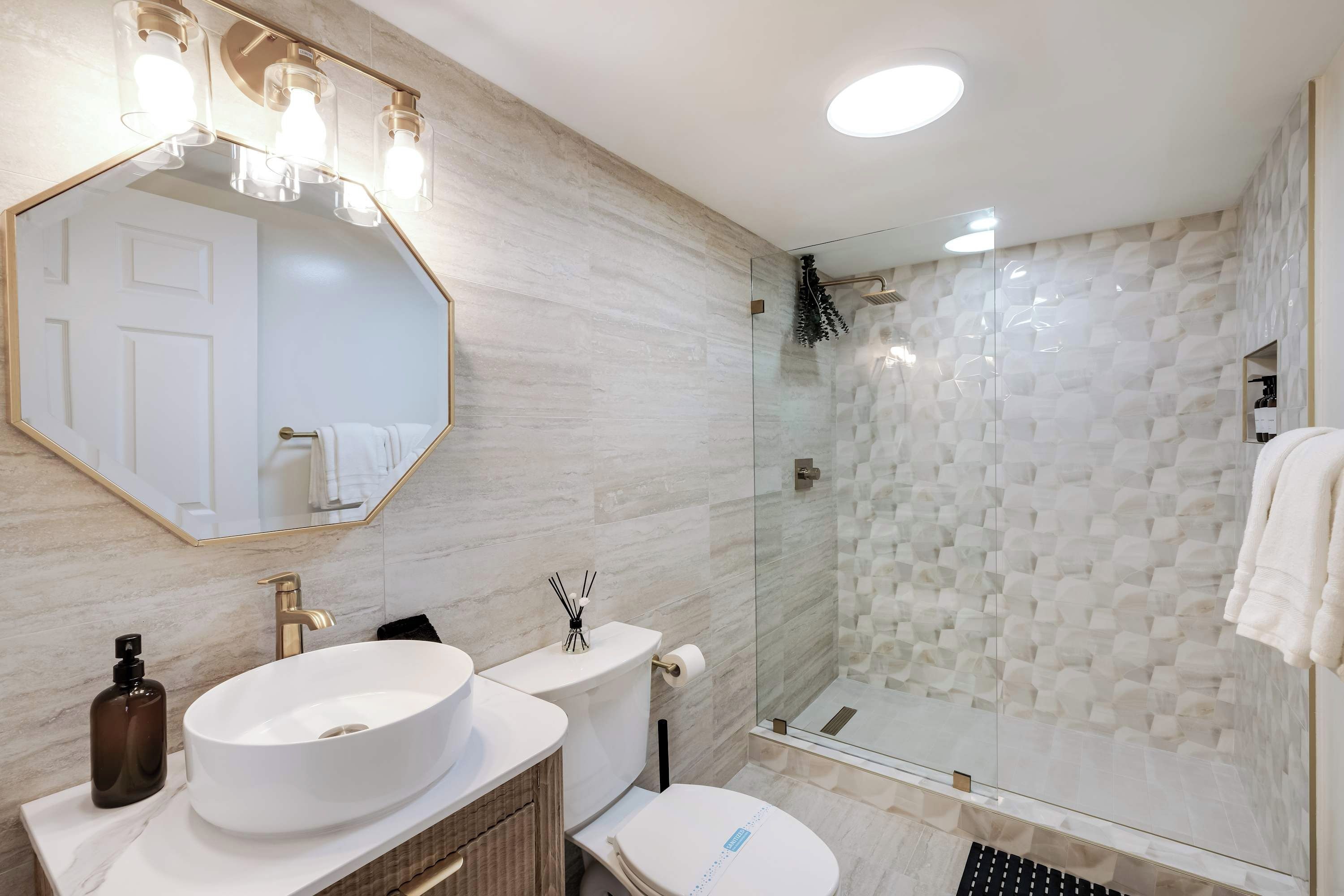 Un baño moderno con un espejo grande, dos lavamanos, un inodoro y una ducha con mampara de cristal.