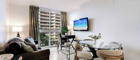 A modern living room with a sofa, a glass dining table, and a TV mounted on the wall.
