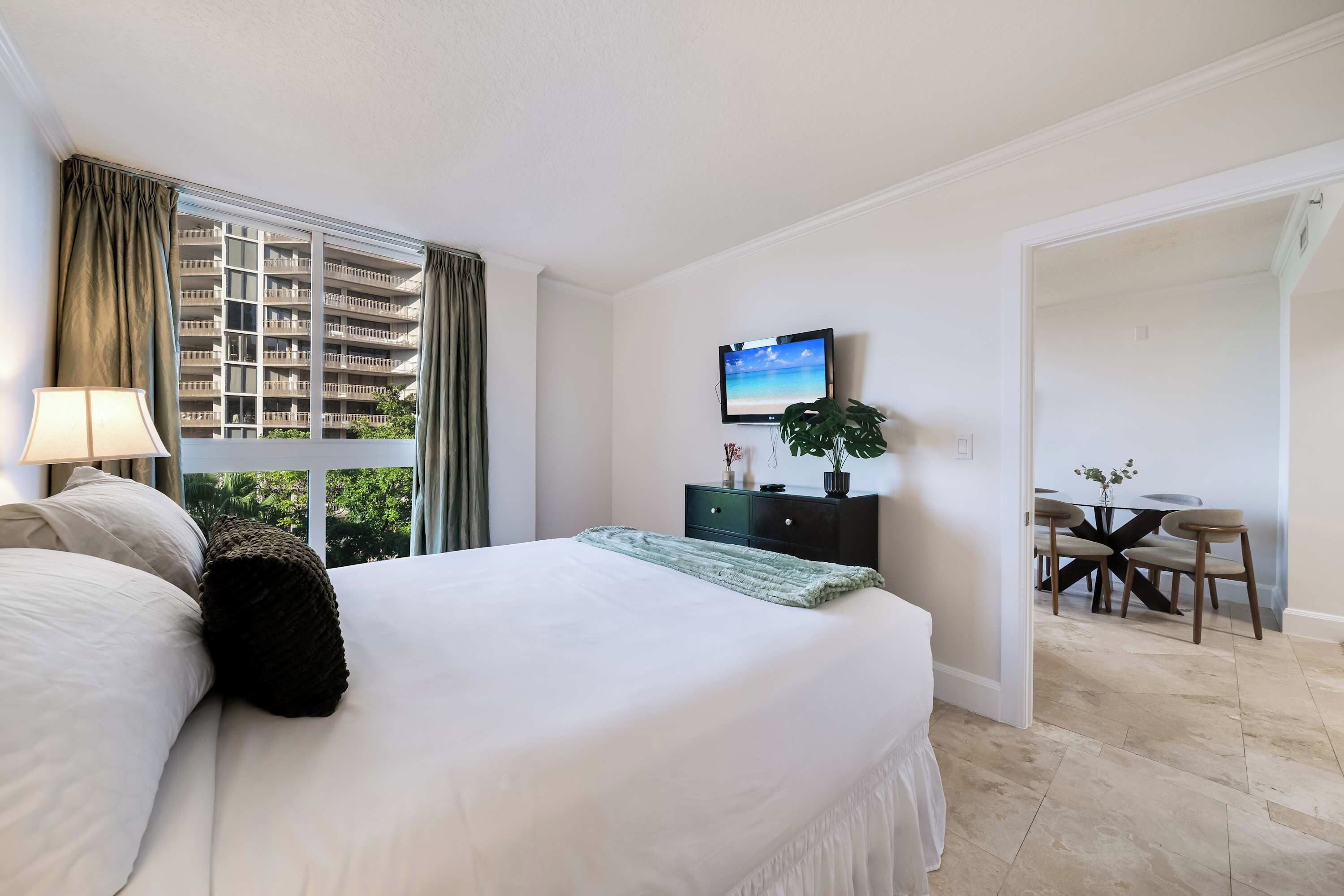 Ein Hotelzimmer mit Bett, Fernseher, Schreibtisch und Blick auf ein Gebäude.