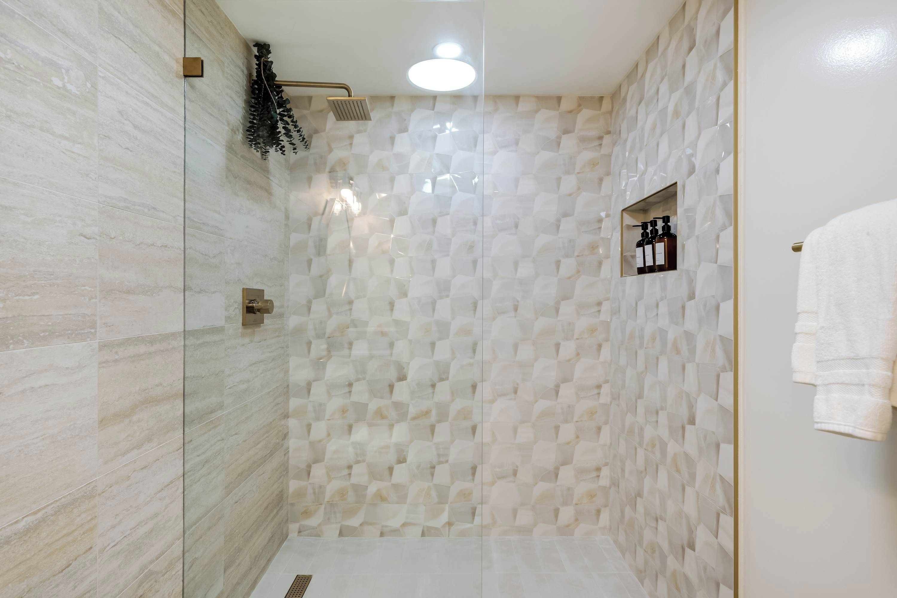 A modern bathroom with a glass shower enclosure, a marble wall, and a small shelf with toiletries.