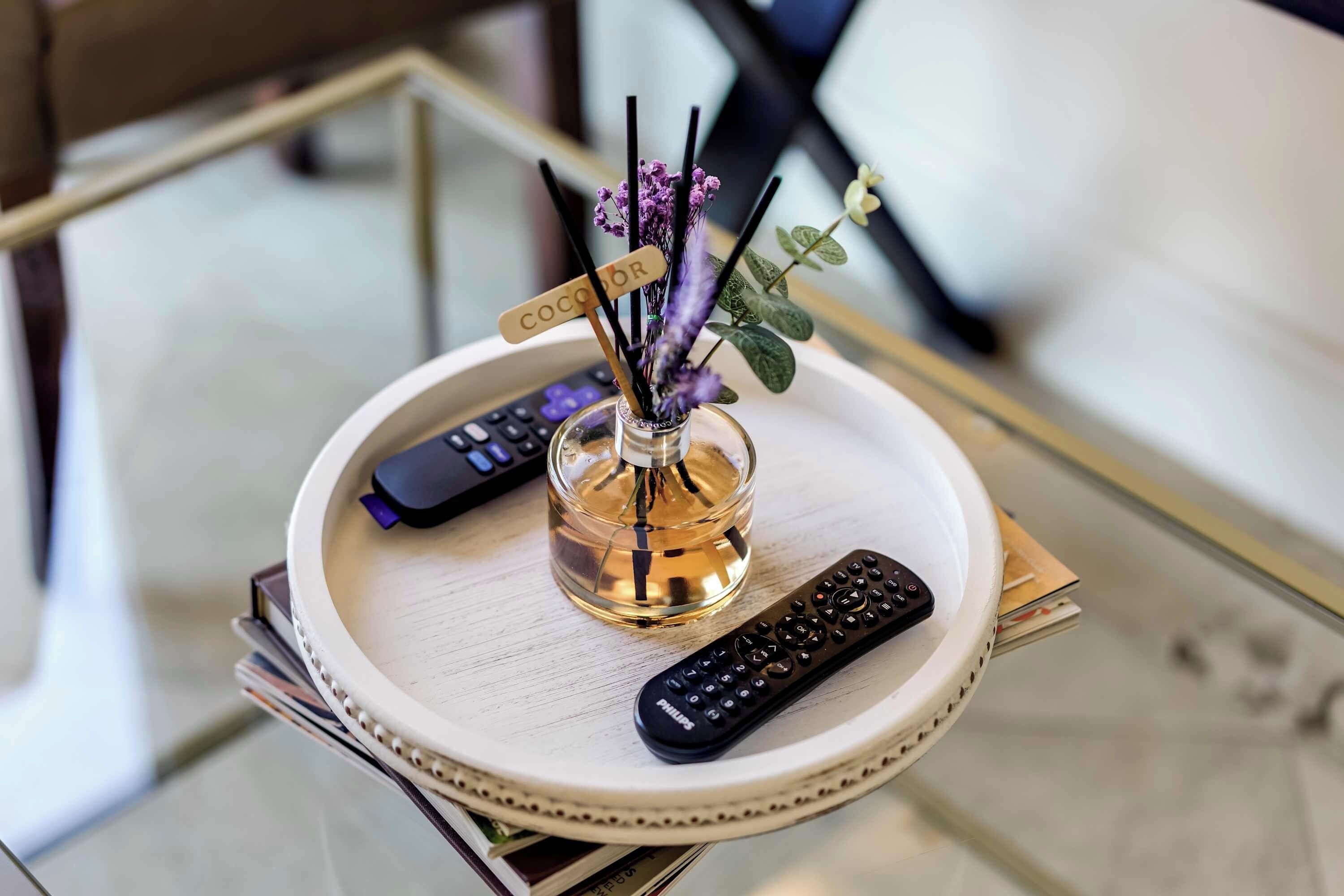 A tray with a remote control, a glass bottle, and a small vase with purple flowers.