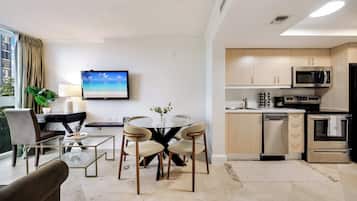 Una sala moderna con una mesa de centro de vidrio, dos sillones, un televisor y una cocina con microondas y horno.