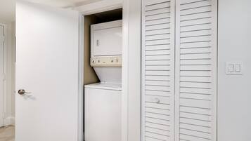 Un cuarto de lavandería con lavadora y secadora, una puerta blanca y un armario blanco con puertas de listones horizontales.