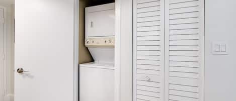 A laundry room with a washer and dryer, a white door, and a white closet with horizontal louvered doors.