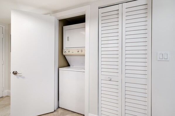 Une buanderie équipée d’un lave-linge et d’un sèche-linge, avec une porte blanche et un placard blanc doté de portes à persiennes horizontales.