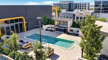Uma área de piscina no terraço com espreguiçadeiras, um espaço de estar coberto e vista para edifícios próximos.