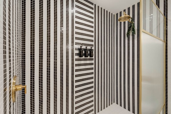 Un baño con pared de baldosas blanco y negro, un cabezal de ducha dorado y un grifo dorado.