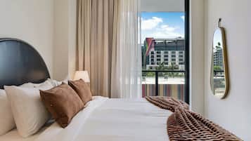 Une chambre d’hôtel avec un lit, des oreillers, une couverture, une fenêtre avec des rideaux et un miroir au mur.