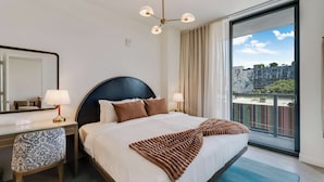 A hotel room with a large bed, a desk with a chair, a mirror, a ceiling light fixture, and a view of the city through a balcony. - Wynwood Pad- Stylish Apt With View & Rooftop Pool (Miami)