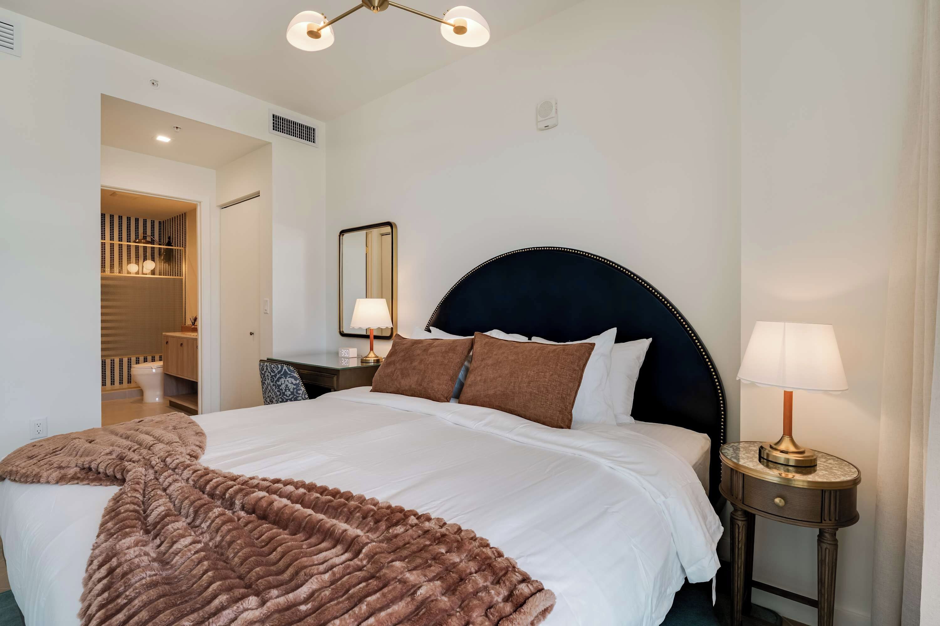 A neatly made bed with a dark headboard, a bedside lamp, and a brown throw blanket.
