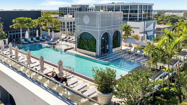 A rooftop pool with lounge chairs and umbrellas, surrounded by palm trees and modern buildings. - Wynwood Pad- Stylish Apt With View & Rooftop Pool (Miami)