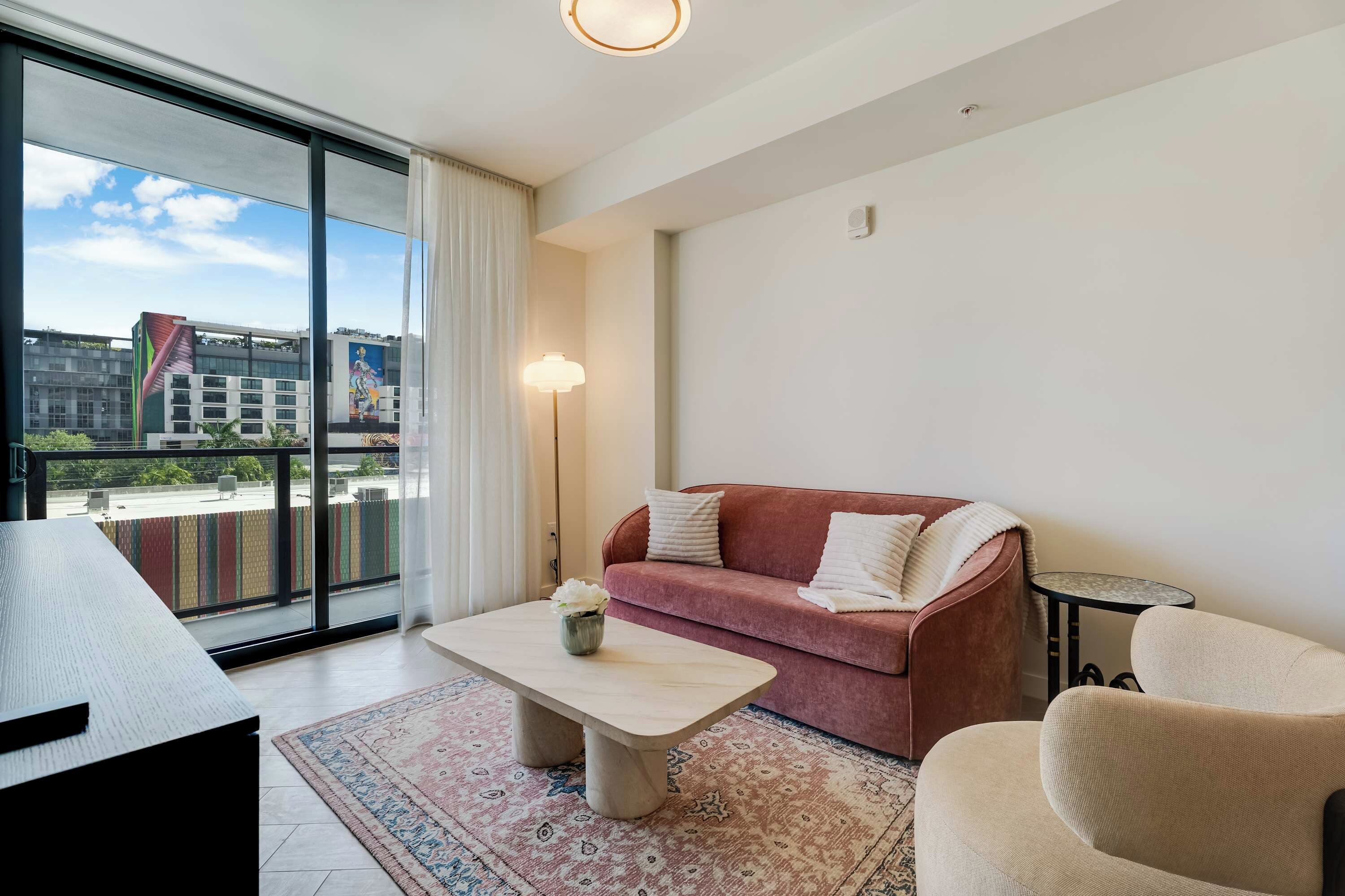 Ein modernes Wohnzimmer mit Sofa, Sessel, Couchtisch und Blick auf Gebäude durch große Fenster.