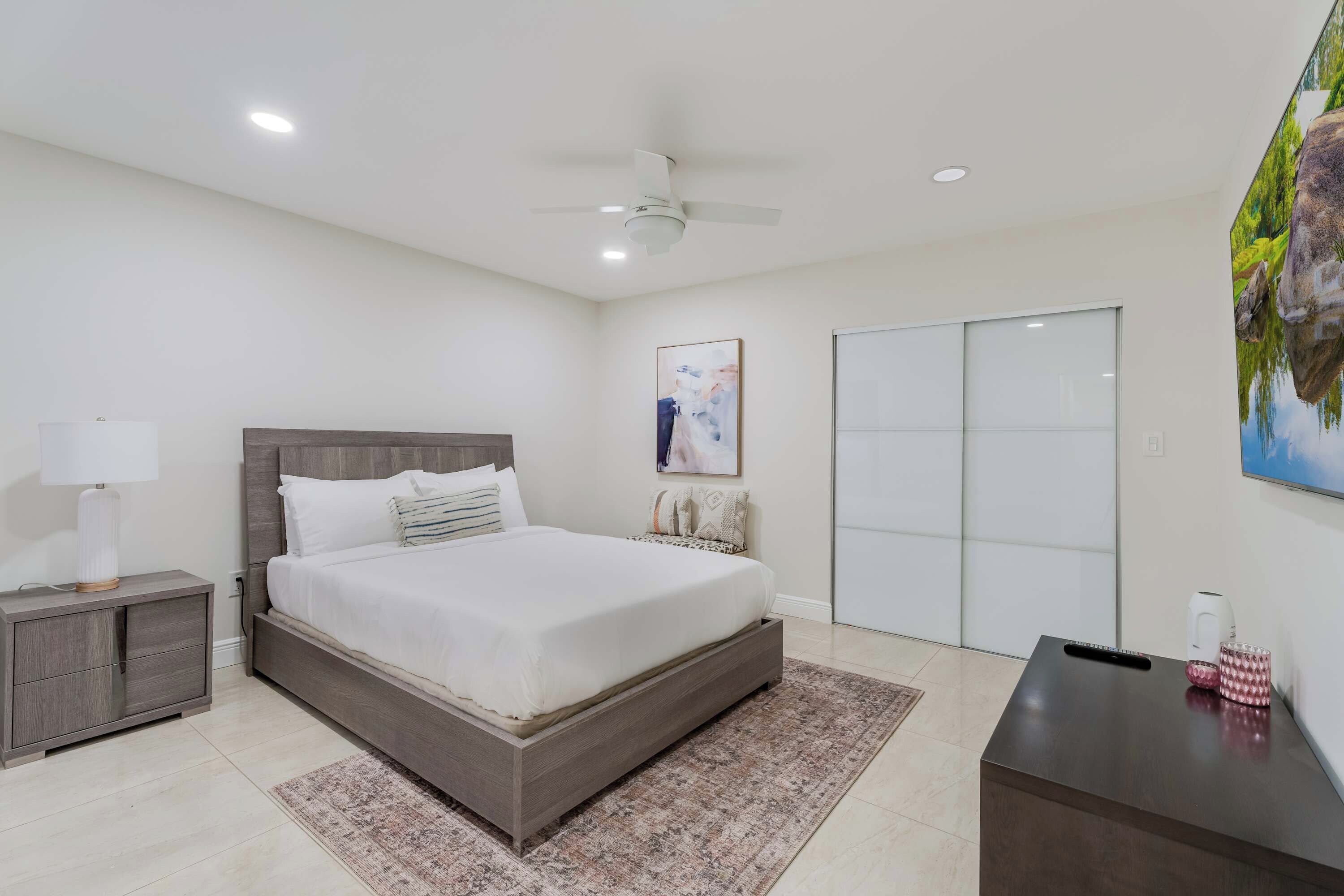 A bedroom with a bed, nightstand, bedside table, and a painting on the wall.