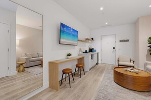 A modern living room with a wooden coffee table, a sofa, a kitchen area, and a large painting of a beach scene. - Brickell Skyline Pool, Gym, and Central Location (Miami)