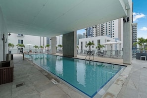 Piscina interior com piso ladrilhado, cadeiras de descanso e vista para edifícios altos.