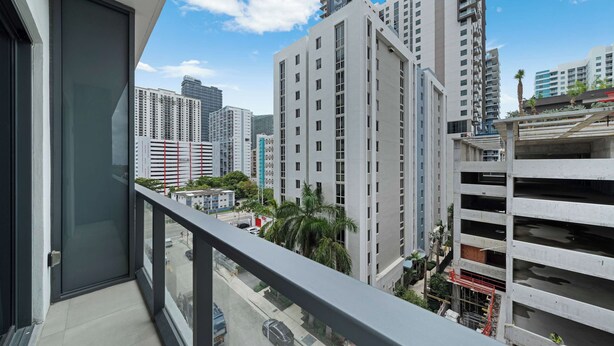 A high-rise building with multiple floors, a balcony with a glass door, and a view of a busy street with cars and palm trees. - Brickell Skyline- Pool, Gym, and Central Location (Miami)