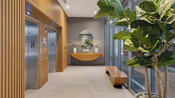 Área de elevador moderna, com painéis de madeira, um balcão de recepção com espelho e um vaso de planta.