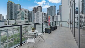 A rooftop terrace with a city view, a table with chairs, and potted plants. - Brickell Skyline- Pool, Gym, and Central Location (Miami)