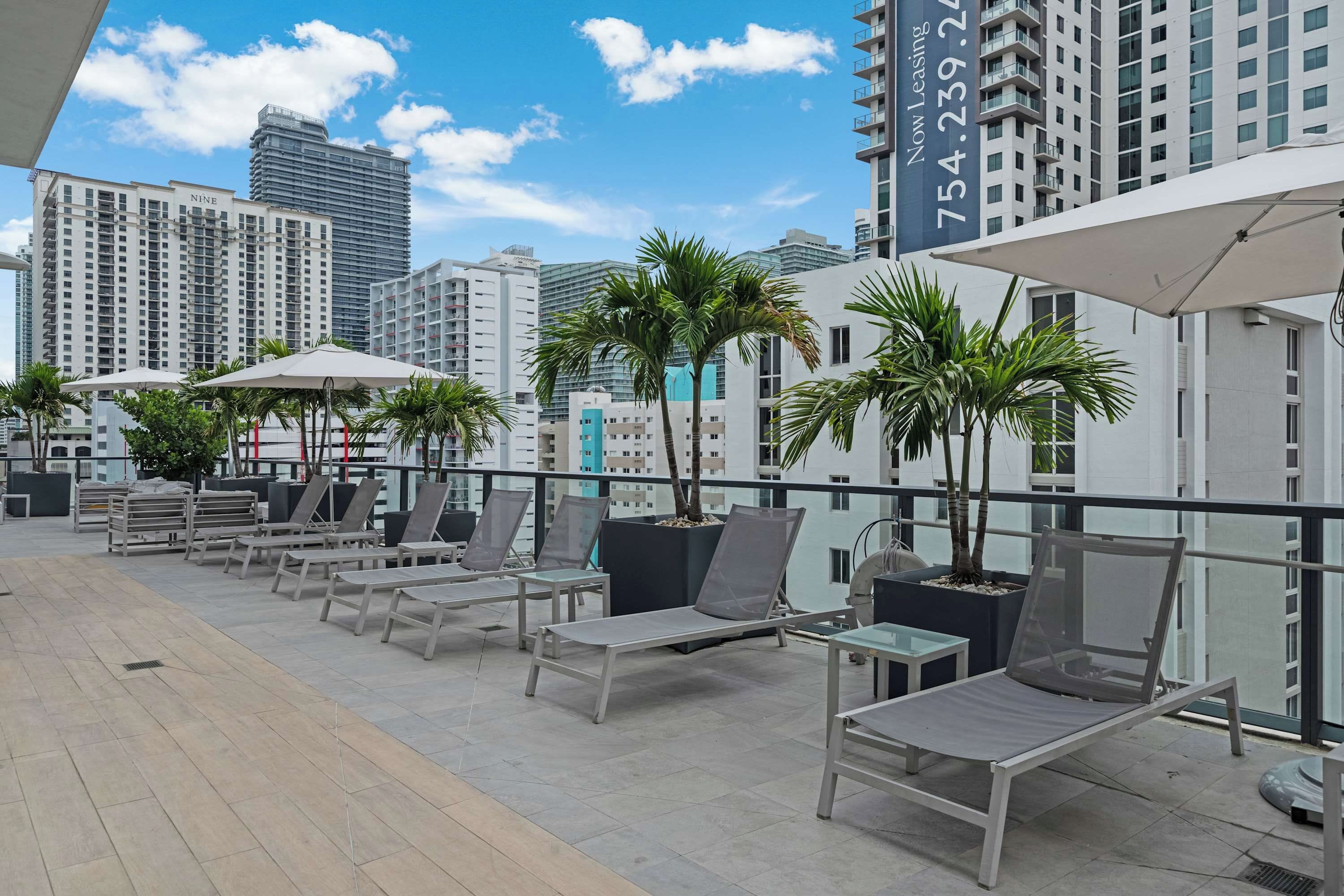 A rooftop terrace with lounge chairs, umbrellas, and potted plants.