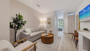 Uma sala de estar moderna com um sofá, uma mesa de centro redonda, uma planta e um quadro na parede.