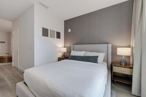 A hotel room with a large bed, two bedside tables with lamps, a wall clock, and a door. - Brickell Skyline Pool, Gym, and Central Location (Miami)