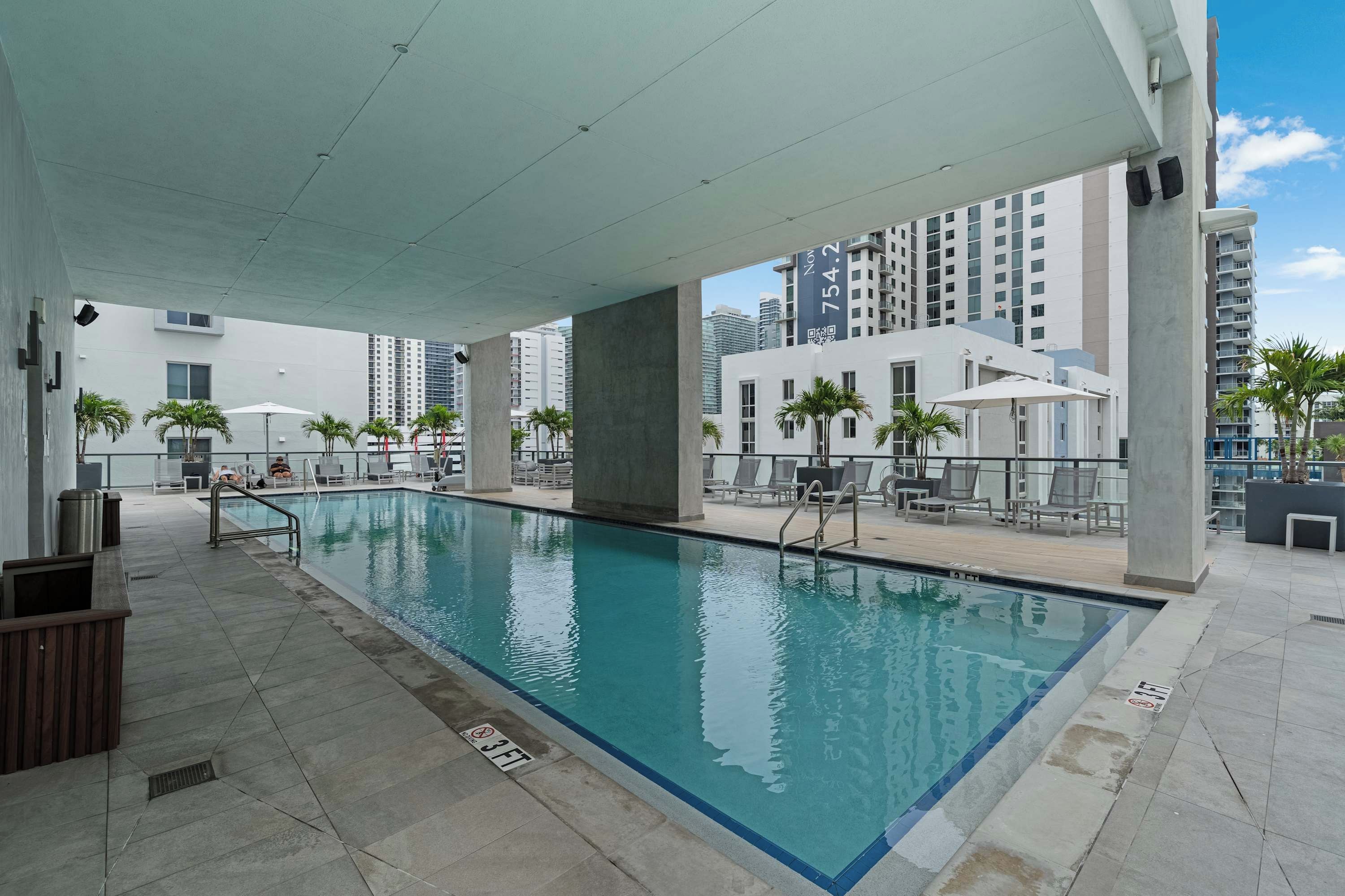 Piscina interior com piso ladrilhado, cadeiras de descanso e vista para edifícios altos.