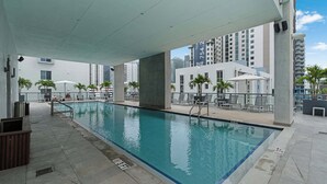 An indoor swimming pool with a tiled floor, lounge chairs, and a view of high-rise buildings. - Brickell Skyline- Pool, Gym, and Central Location (Miami)