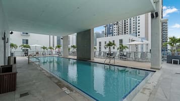 Piscina interior com piso ladrilhado, cadeiras de descanso e vista para edifícios altos.