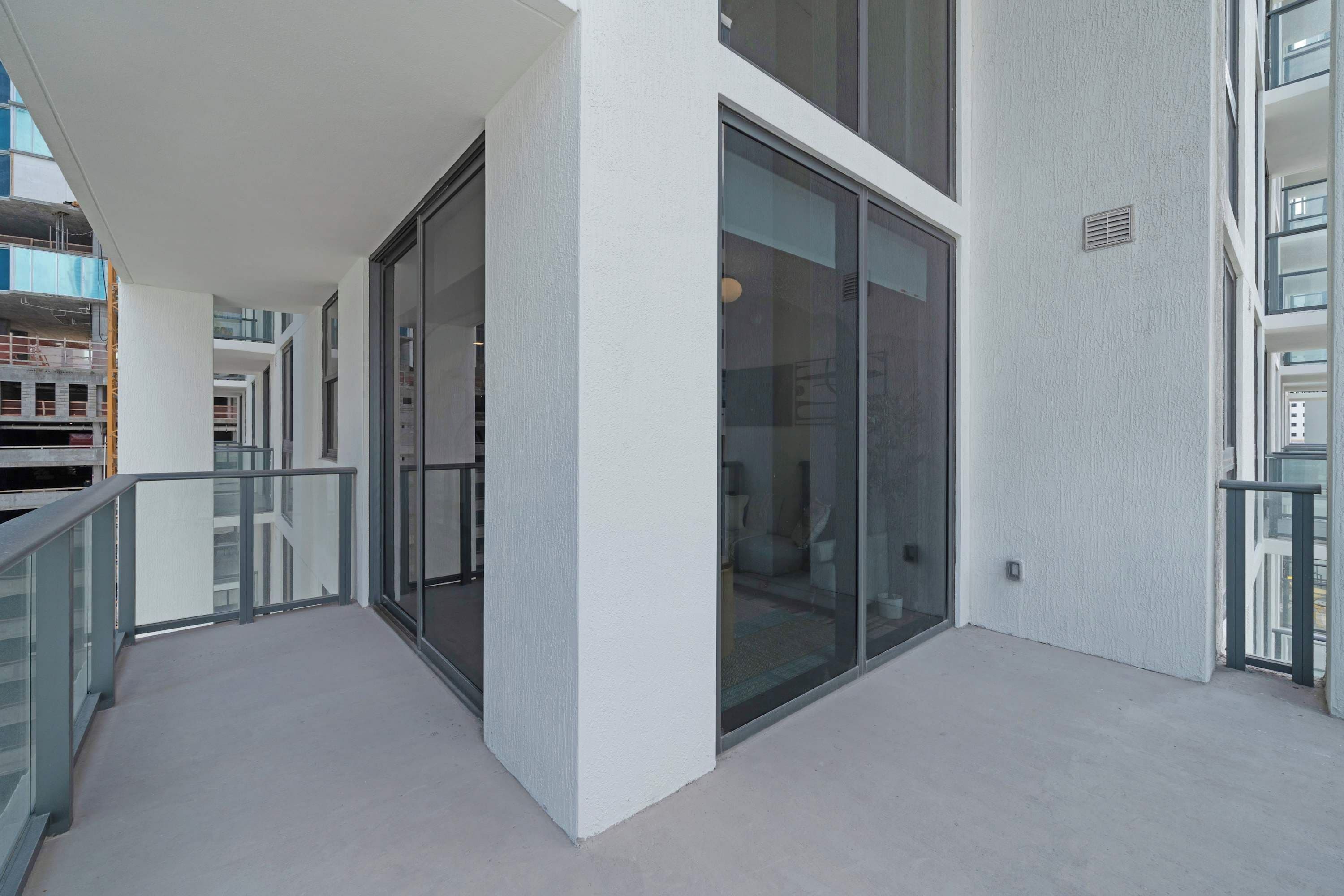 A modern building with large glass windows, a balcony with a metal railing, and a concrete floor.