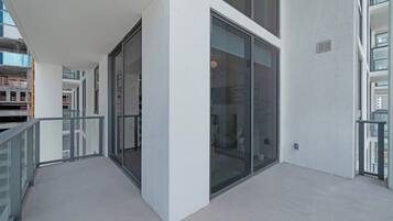 A modern building with large glass windows, a balcony with a metal railing, and a concrete floor.