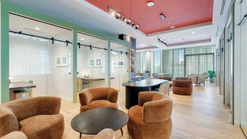 A modern office space with glass partitions, brown upholstered chairs, a central black table, and a red ceiling.
