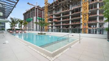 Une piscine dotée d’une terrasse carrelée, entourée d’un bâtiment en construction, composé de plusieurs étages et entouré d’échafaudages.